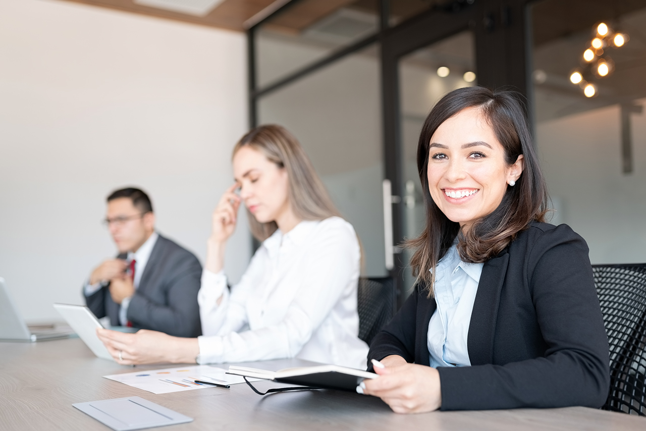 Portrait of beautiful young caucasian businesswoman sitting at conference table with colleagues at the back during meeting