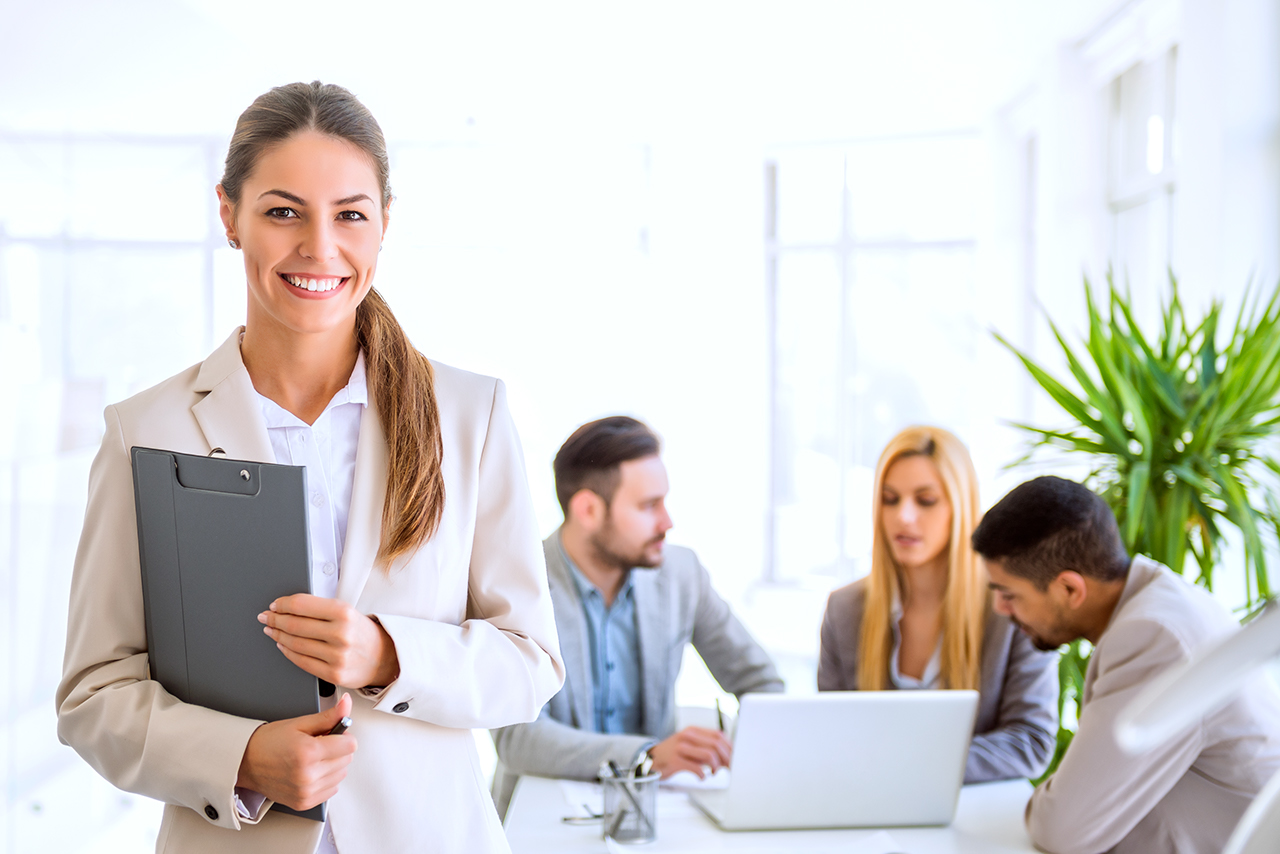 Smiling businesswoman standing with colleagues in the background.